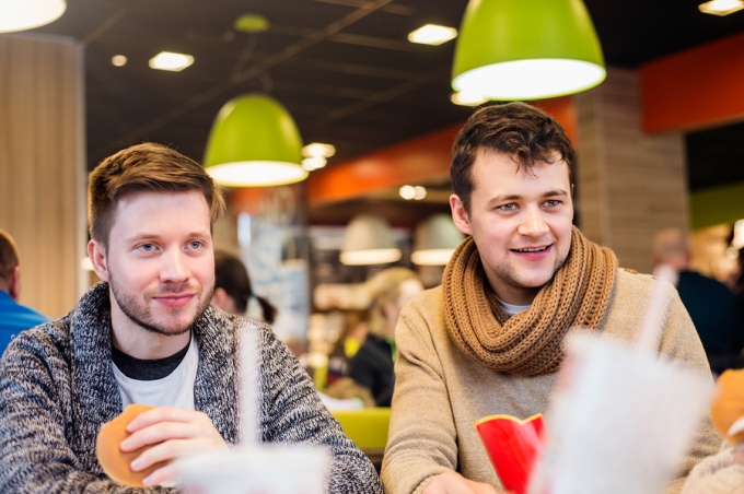 Two young men eating out in fast food restaurant, talking, having fun